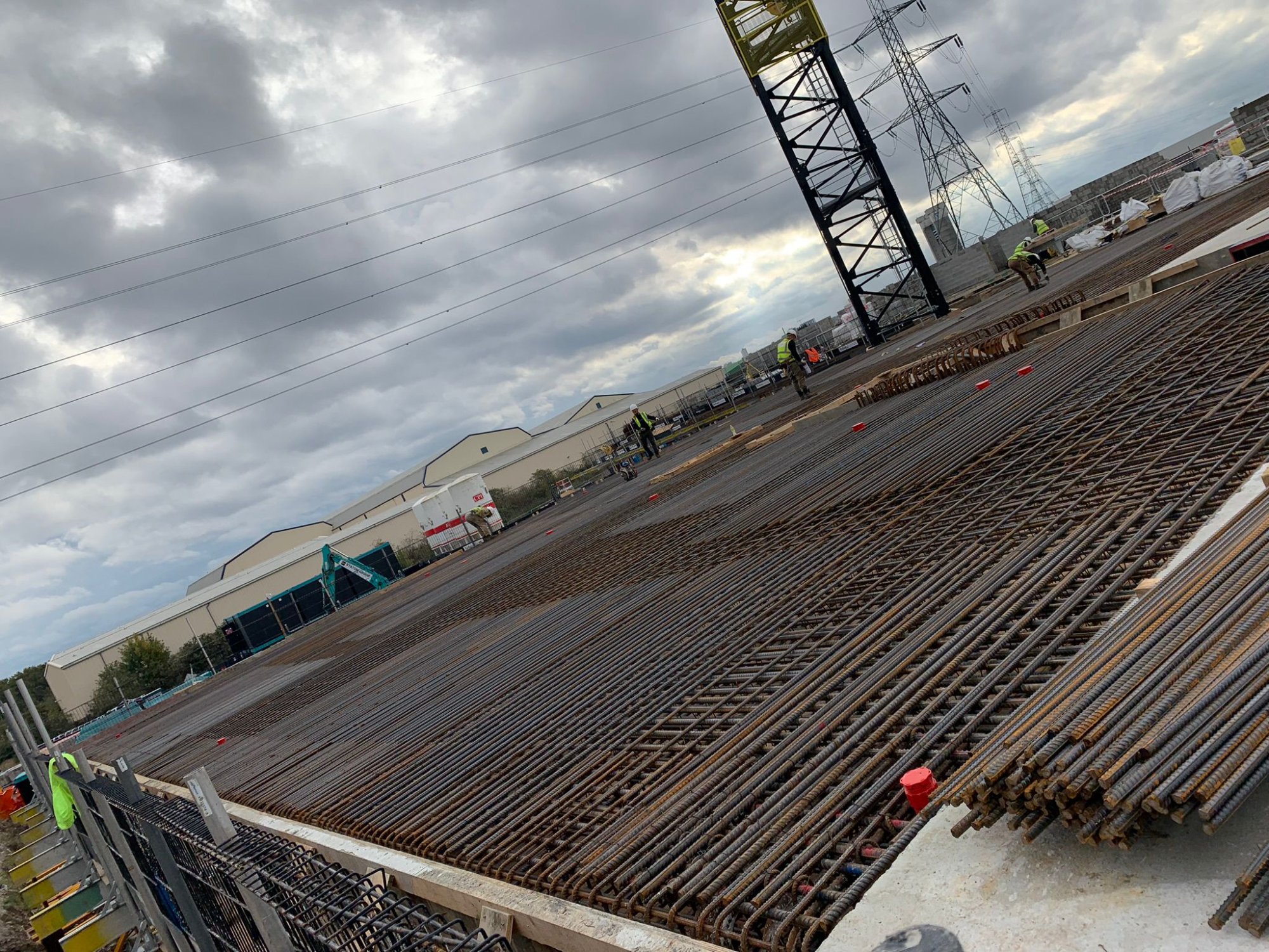 Ground-level rebar grid with workers preparing post-tensioning at Canary Wharf